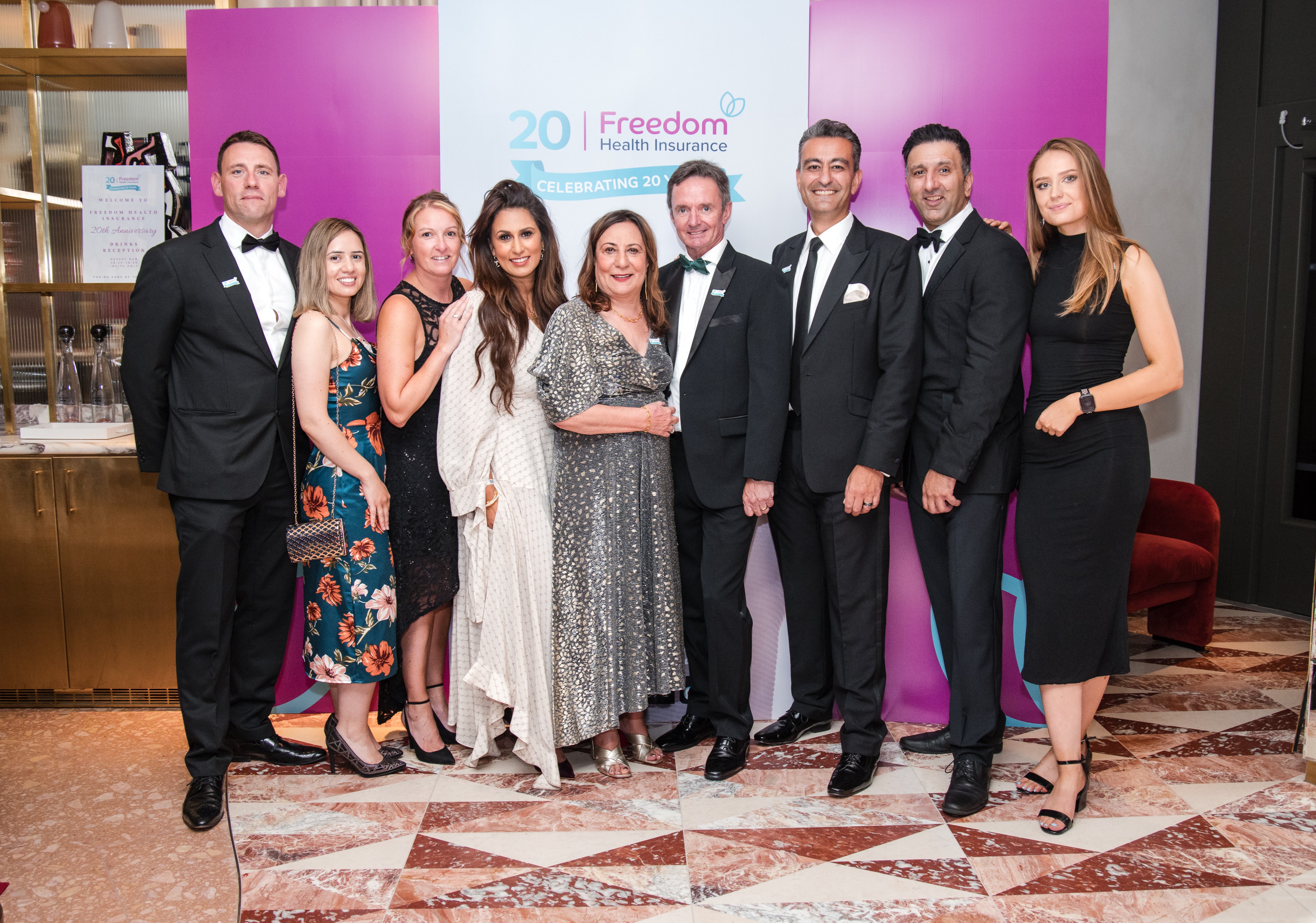 Members of the Freedom Health Insurance team at the company's 20th anniversary celebration, in front of a Celebrating 20 Years banner